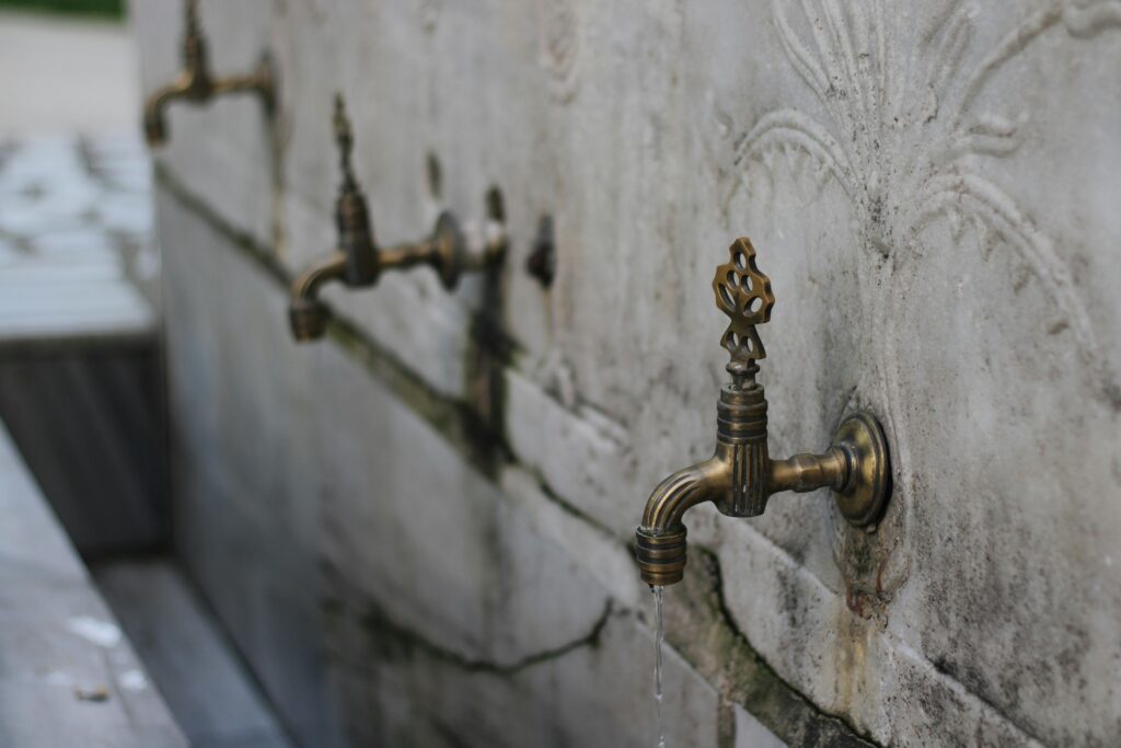 Close-up of antique brass tap in mosque ablution area on decorative stone wall.