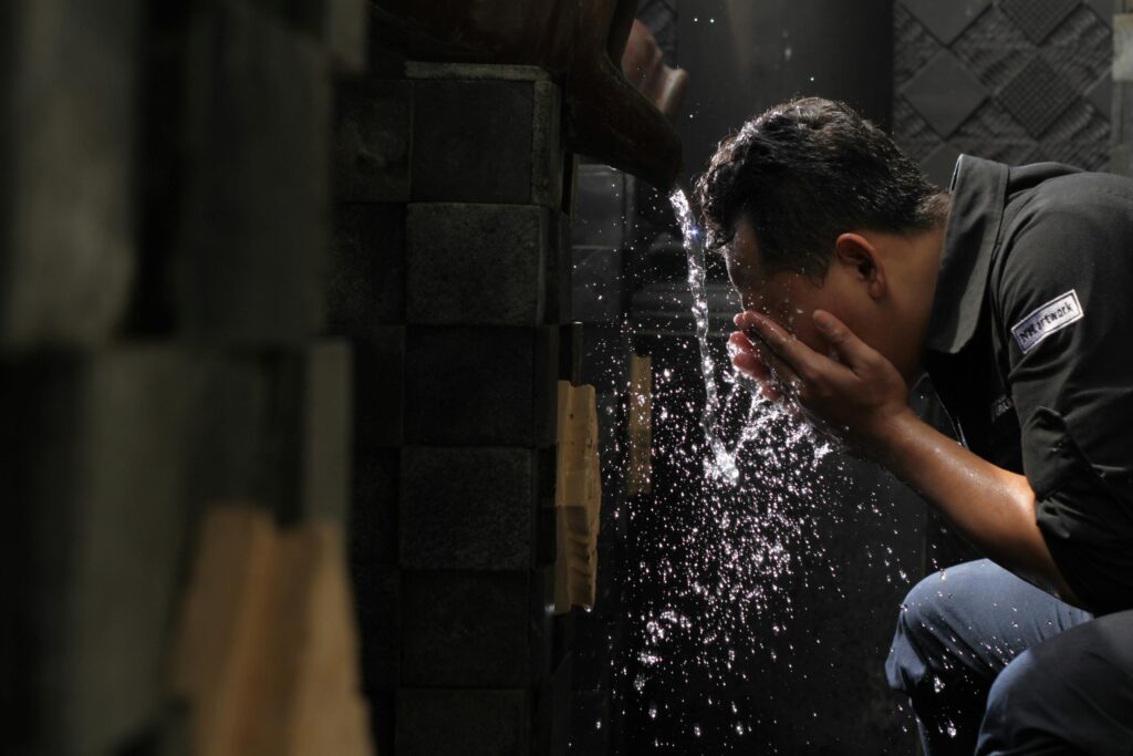 A man washes his face with flowing water indoors, highlighting daily hygiene and refreshment.