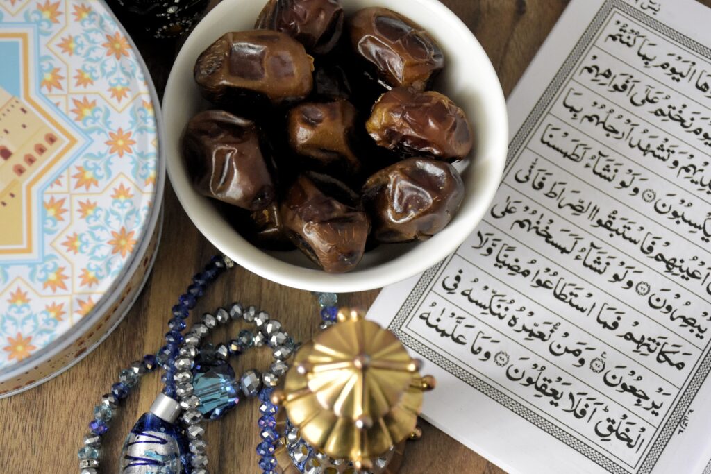 A bowl of fresh dates beside open Quran, symbolizing Ramadan fasting traditions.